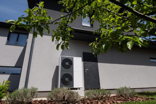 The wall of a modern cottage hosts the outdoor unit of a heat pump. High quality photo